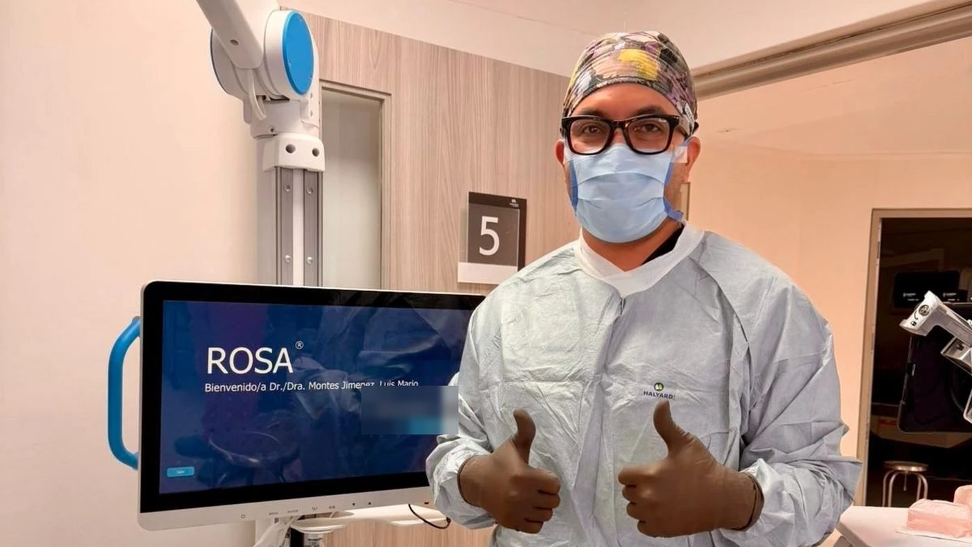 El Dr. Luis Mario Montes en quirófano junto al sistema robótico ROSA, con su nombre en la pantalla de bienvenida